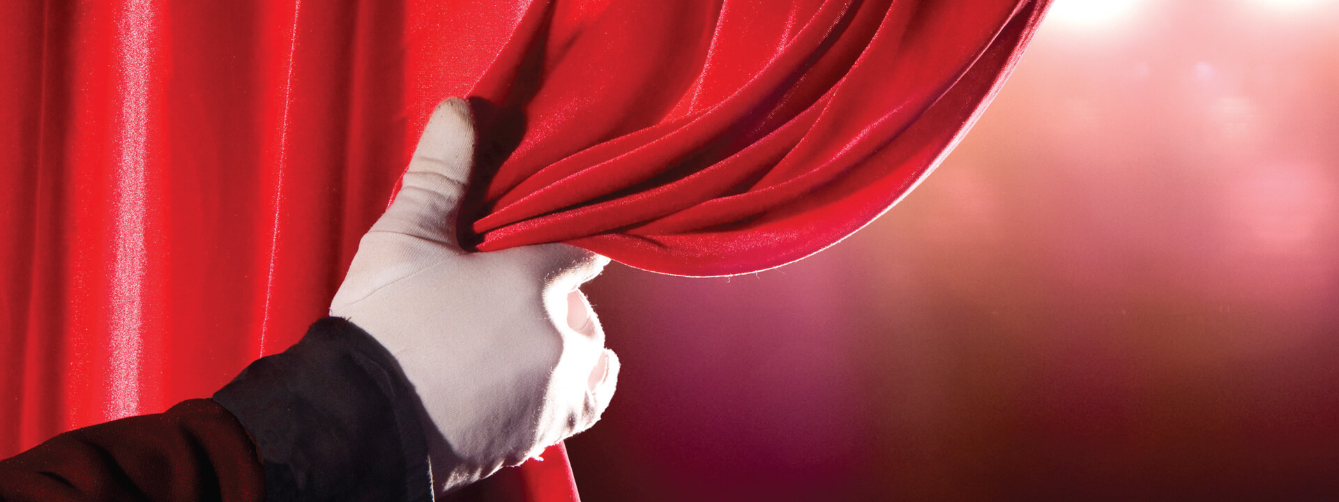 Close up of a gloved hand pulling back a stage curtain