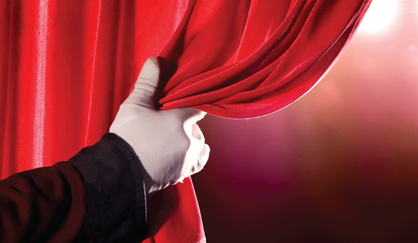Close up of a gloved hand pulling back a stage curtain